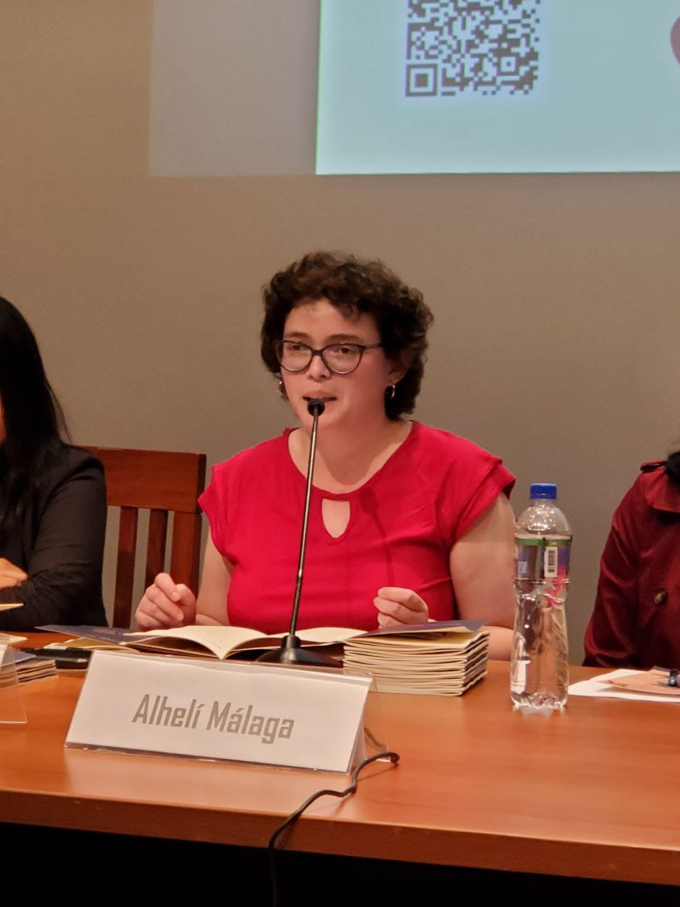 Alhelí Málaga, con cabello corto y un vestido rojo, se dirige al público