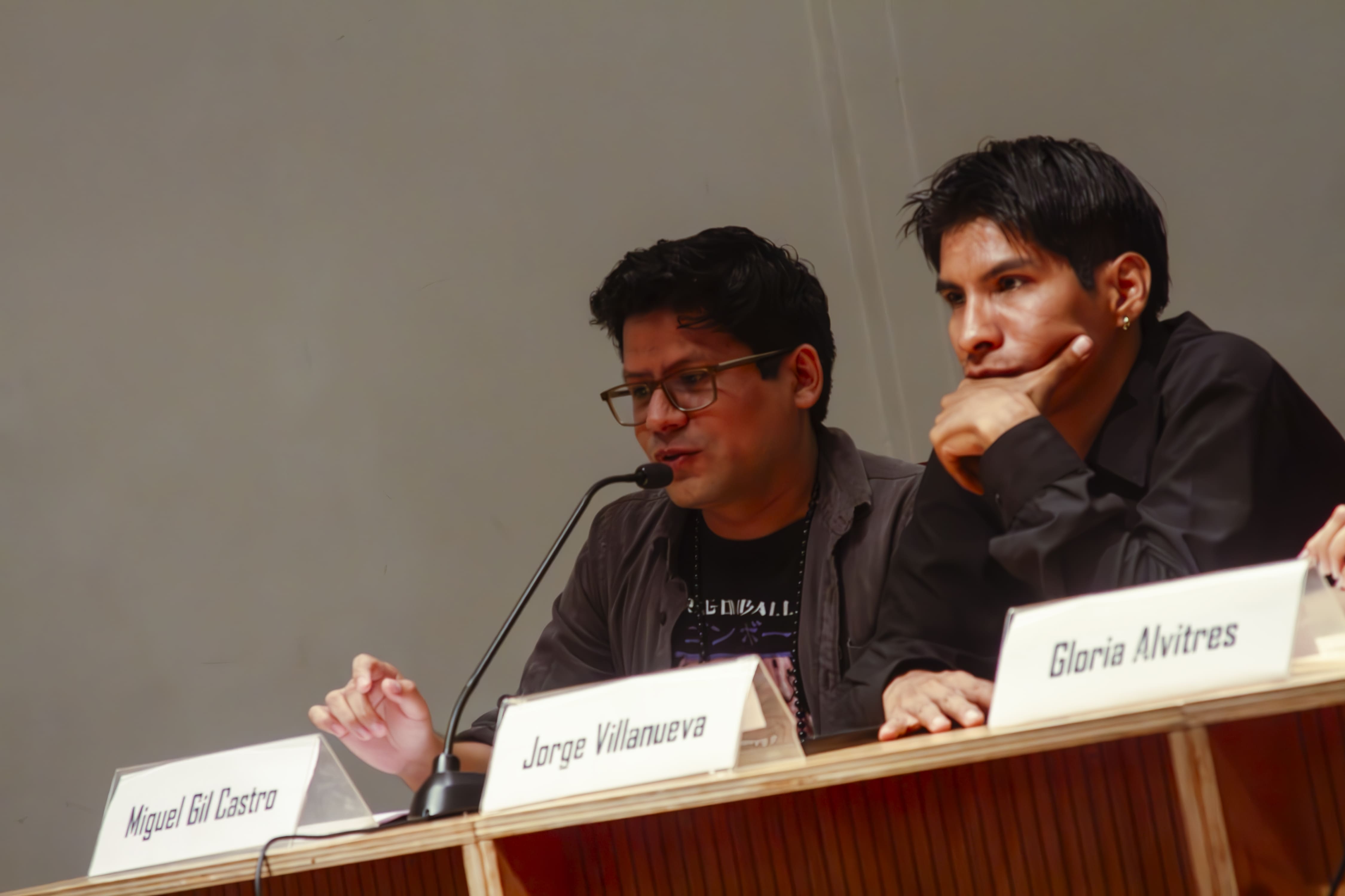 Miguel Gil está leyendo sus poemas como parte de la mesa de presentación con una ligera sonrisa, a su lado derecho está Villanueva Lorenzo, muy concentrado