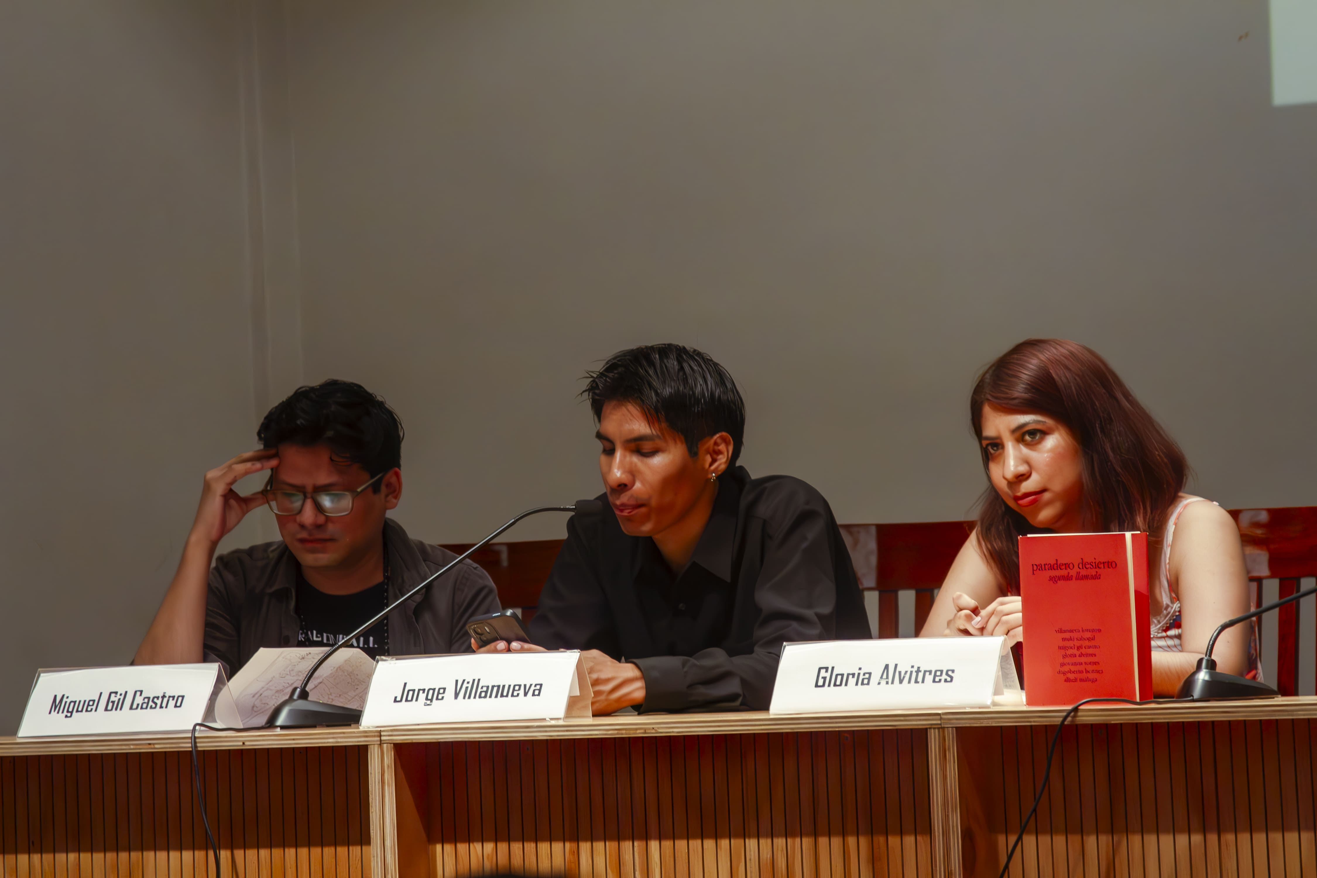 Villanueva Lorenzo lee algunos poemas como parte de la mesa de presentación, a su izquierda está Miguel Gil, y a la derecha Gloria Alvitres